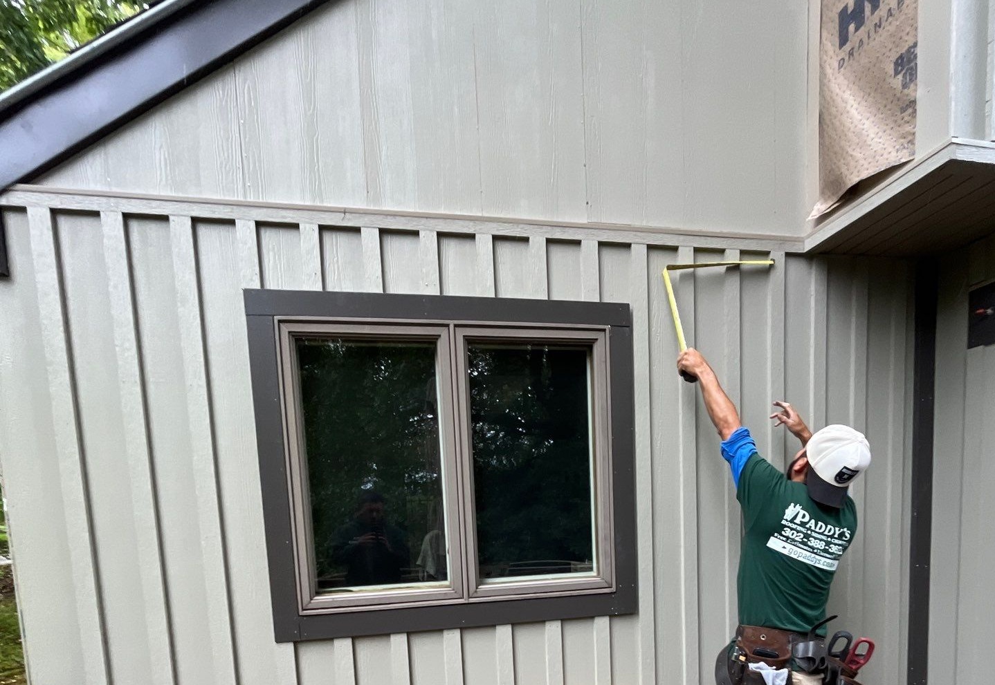 Paddy's siding expert measuring beige fiber cement siding at a job site.