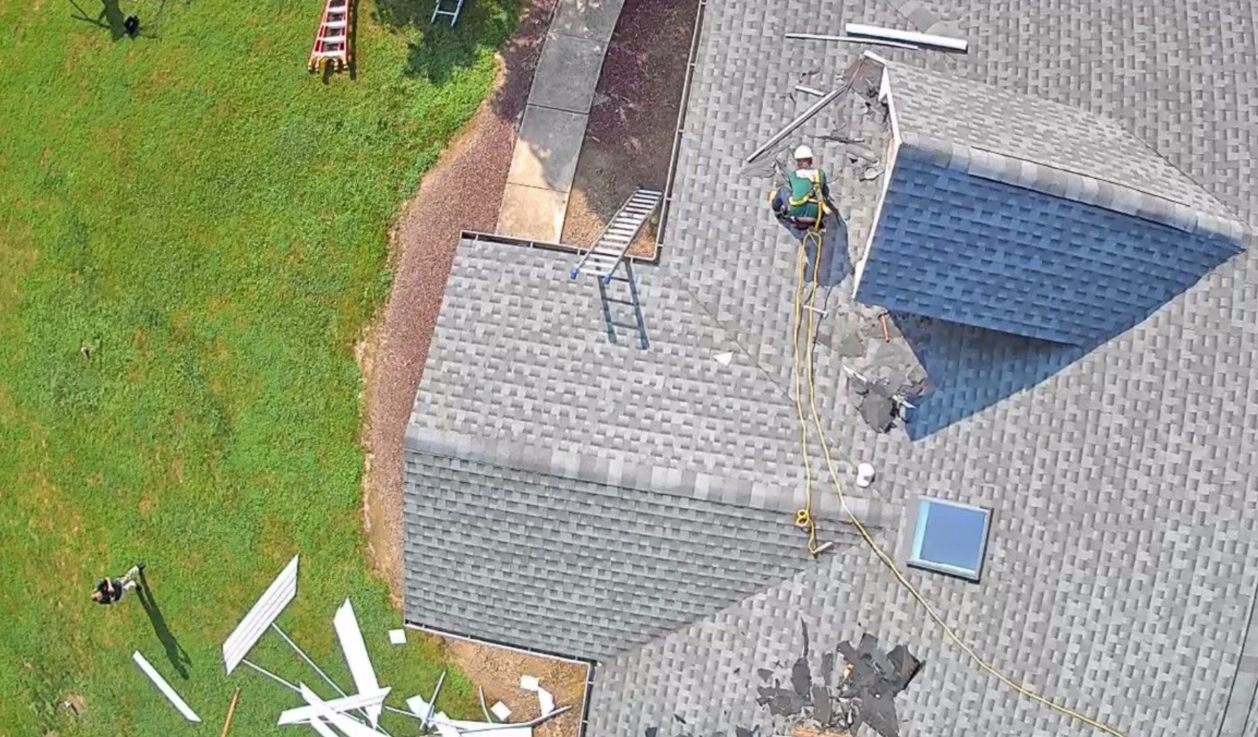 View from above of a Paddy's roofer working on a new light gray shingle roof with green lawn around below