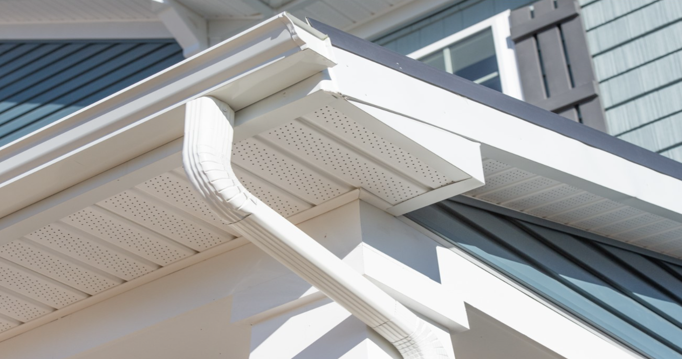 Closeup of white soffit, fascia and downspout on house with gray siding